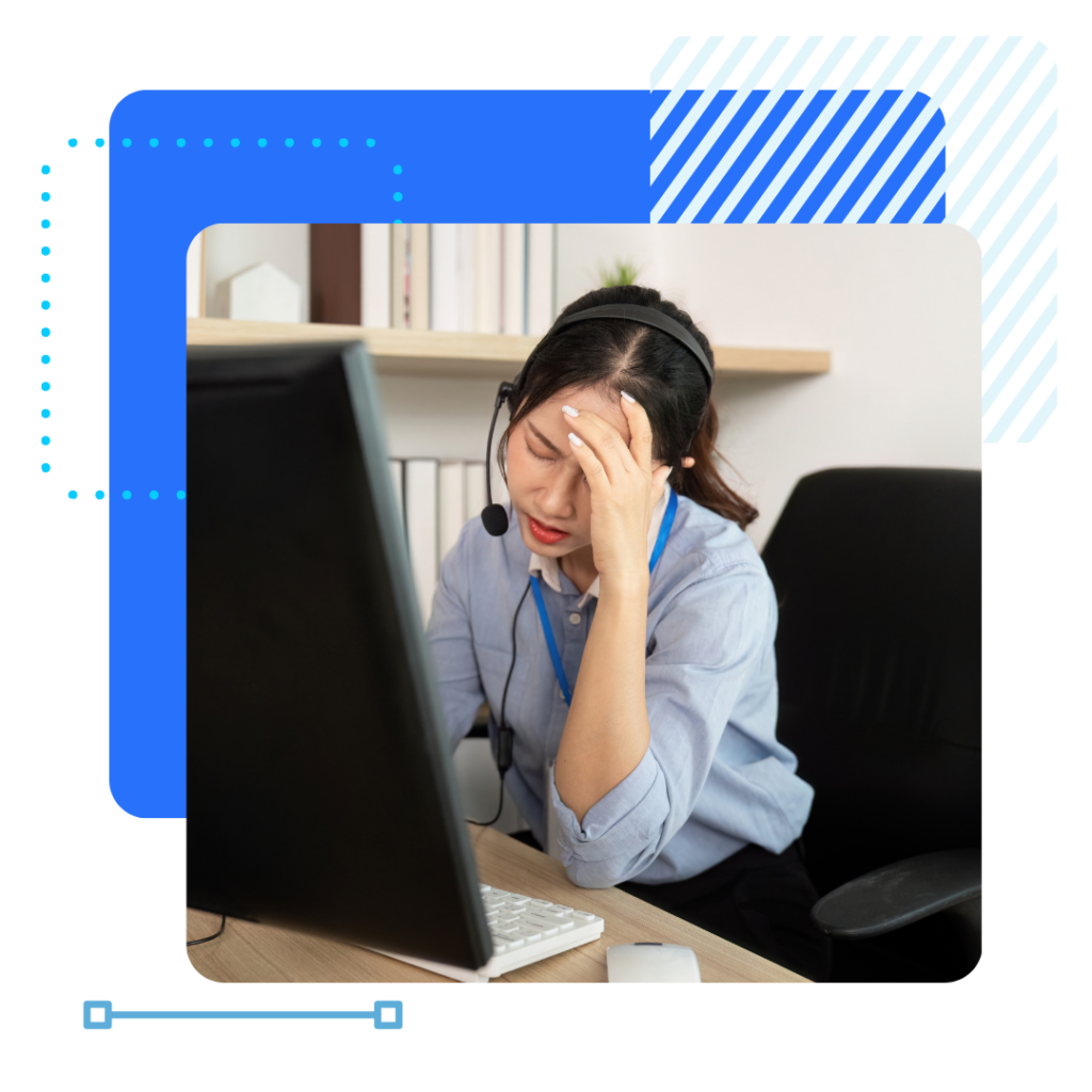 A person wearing a headset sits at a desk, resting their head on one hand, appearing stressed while looking at a computer monitor.
