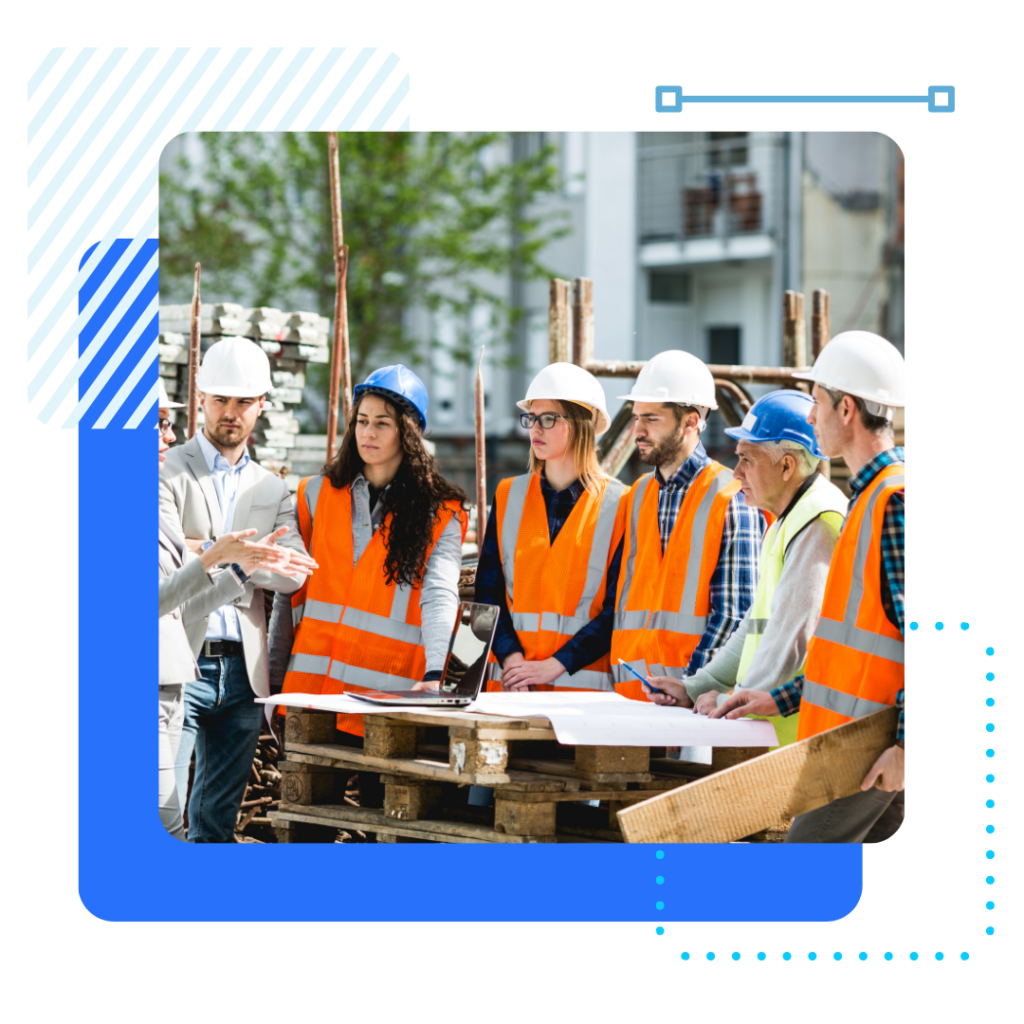 A group of construction workers and a supervisor in hard hats and reflective vests stand around a table with blueprints, discussing plans.