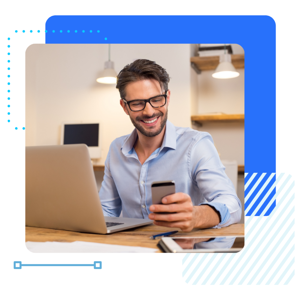 An insurance man with glasses sits at a desk, holding a smartphone. A laptop is open in front of him.