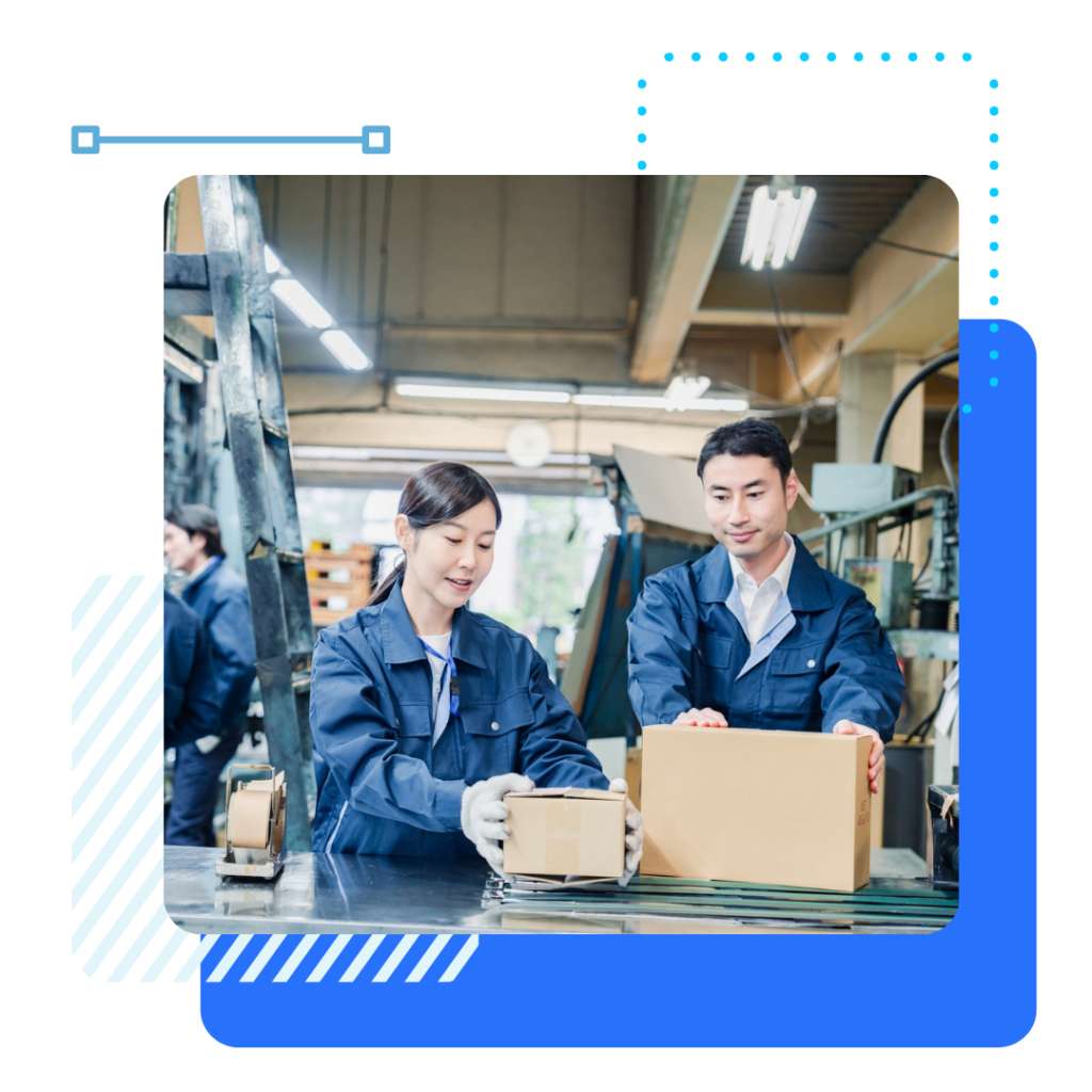 Two manufacturers in blue uniforms handle packages in a well-lit factory. They appear focused and collaborative.
