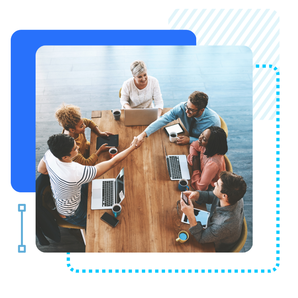 A diverse group seated around a wooden table in a modern office setting, smiling and shaking hands. Laptops, coffee mugs, and a collaborative atmosphere.